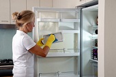 Женщина моет холодильник